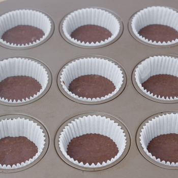 chocolate battered cupcakes in a muffin tin ready to bake.