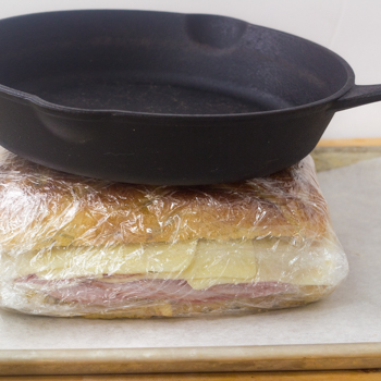 Sandwich being pressed down by cast-iron skillet.