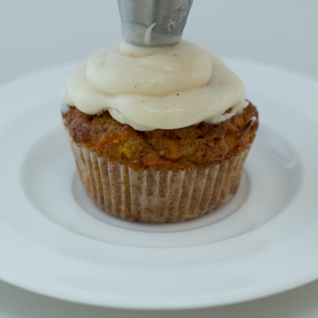 Piping cream cheese frosting onto muffin,